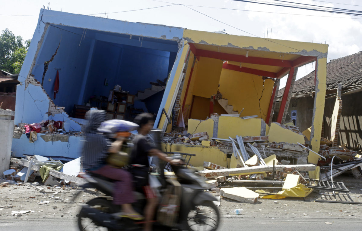 A motorcycle passes buildings destroyed by Sunday's earthquake in North Lombok, Indonesia, Friday, Aug. 10, 2018. The north of Lombok was devastated by the powerful quake that struck Sunday night, damaging thousands of buildings and killing a large number of people. (AP Photo/Firdia Lisnawati)