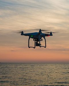 Drone floats over sea with sunset in background